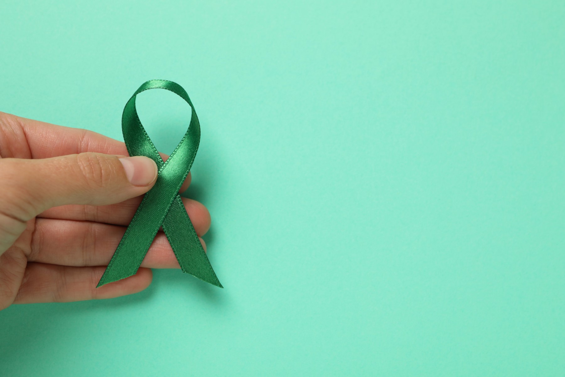 glaucoma awareness month female hand holding green awareness ribbon on mint background